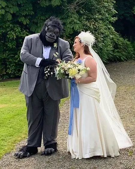 Jorge in a Gorilla costume below his suit while his wife looks at him with a bouquet in his hands.