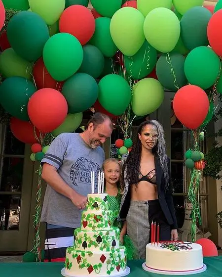 Boogie dressed as Batman's nemesis 'Two-Face' (right), Betty as 'Poison Ivy' (center) and trey is just in normal home clothes laughing at something and looking down. The are pictured behind two cakes and balloons in the background.