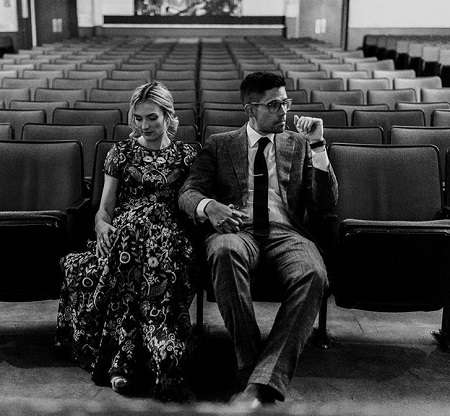 Julie Nolke and husband Sam Larson holding hands during their wedding day sitting in an empty hall.