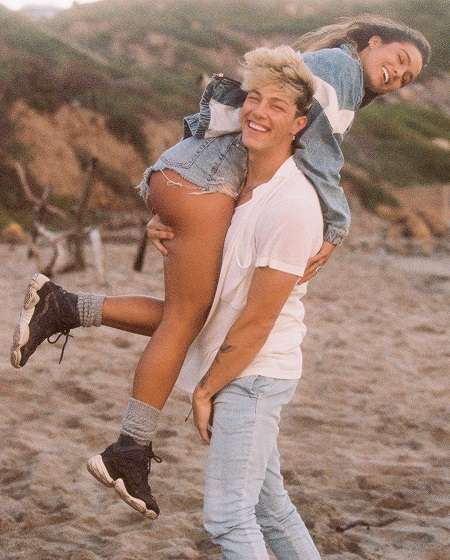 Tayler Holder carrying his GF Sommer Ray on the beach, with smiles.