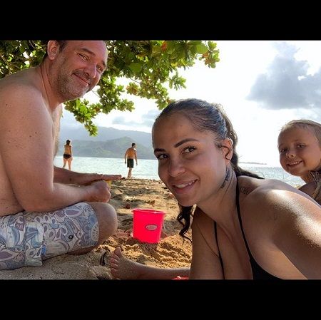 Boogie clicking selfie in a beach with Trey (left) smiling and facing 90 degrees away from camera, but face still facing it and Betty's head is popping in the right behind Boogie, smiling.