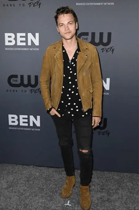 Alexander Calvert in front of The CW banner promoting 'Supernatural.'